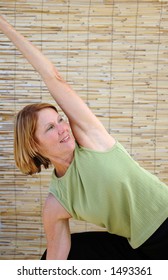 Senior Woman In The Warrior Angle Pose, Virabhadra, With A Natural Bamboo  Backdrop.