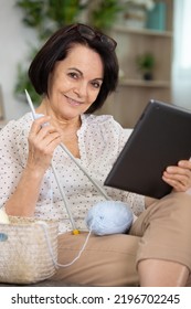 Senior Woman Watching Series Online On Electronic Device And Knitting