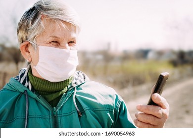 Senior Woman Wearing Face Mask During Corona Virus And Flu Outbreak And Talk With Her Daughter By Cellphone. Surgical Masks For Coronavirus Prevention For Old People. Look To The Camera