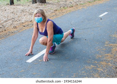 Senior Woman Wearing A Medical Mask Is Runn In A Start Position Outdoors In The Park On A Treadmill. Enjoying A Summer Day In The Nature. Health Of The Elderly.