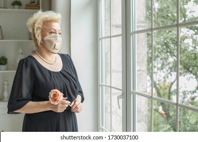 Senior Woman Wearing Protective Mask And Black Dress Looking At The Window At Home