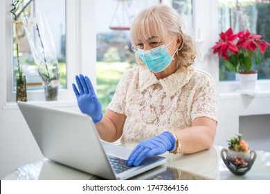 Senior Woman Wearing Protective Mask And Blue Latex Gloves Waving Hand And Greeting Family Members During Video Call On Laptop.