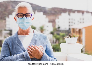 Senior Woman Wearing Surgical Mask Greets With Her Hand Over The Heart. The New Greeting Recommended By The World Health Organisation Due To The Coronavirus Covid-19 Pandemic