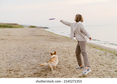 Senior woman wearing sweater playing with her dog on sandy beach