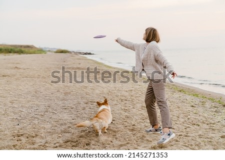 Senior woman wearing sweater playing with her dog on sandy beach