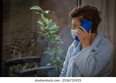 Senior woman wears a protective face mask in quarantine using smartphone at home - Powered by Shutterstock