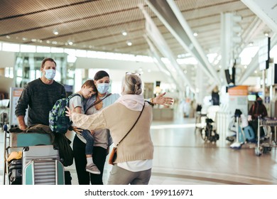 Senior Woman Welcoming Her Daughter And Family  With Open Arms At Airport Arrival Gate. Traveler Family Of Three Welcomed By Grandma At Airport In Pandemic.