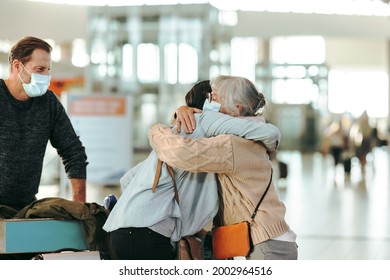 Senior woman welcoming her daughter arriving at airport after pandemic. Woman greeting her mother at airport arrival while her husband looks. - Powered by Shutterstock