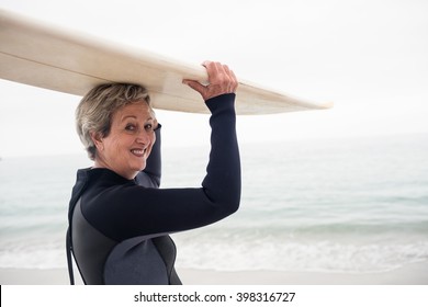 Senior woman in wetsuit carrying surfboard over head on the beach - Powered by Shutterstock