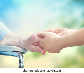 Senior Woman In Wheel Chair Holding Hands With Young Caretaker