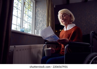 Senior Woman In Wheelchair With Energy Bill By Radiator In Cost Of Living Energy Crisis