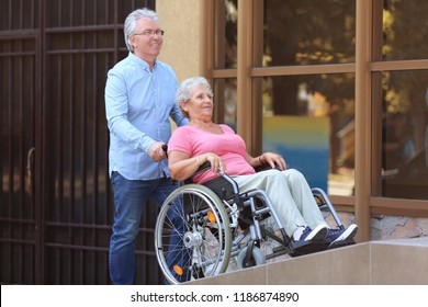 Senior Woman In Wheelchair And Her Husband On Ramp Outdoors