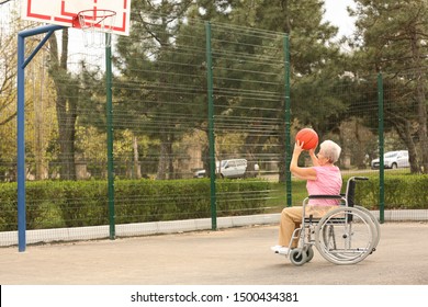 Senior Woman In Wheelchair Playing Basketball On Sports Ground