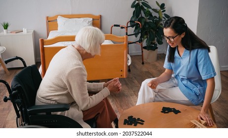 Senior Woman In Wheelchair Playing Dominoes With Happy Nurse