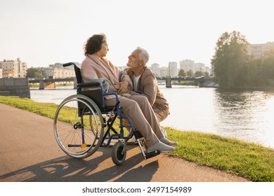 Senior woman in wheelchair walking with caregiver old man on road. Elderly family couple man supporting taking care of paralyzed woman in chair for people with disability outdoor. Rehabilitation - Powered by Shutterstock