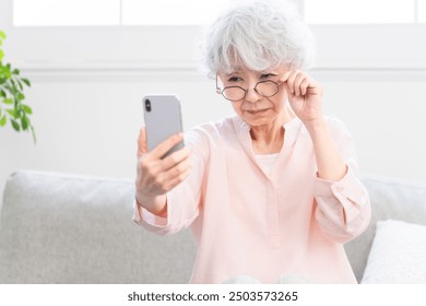 A senior woman who has presbyopia and has trouble seeing her smartphone - Powered by Shutterstock