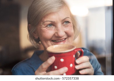 Senior woman at the window holding a cup of coffee - Powered by Shutterstock