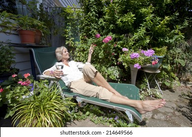 Senior Woman With Wineglass Relaxing On Lounge Chair In Garden