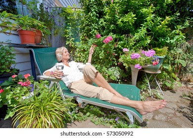 Senior Woman With Wineglass Relaxing On Lounge Chair In Garden