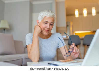 Senior Woman Working On Home Finance. Mature Woman Checking Bills At Home. Older Woman Checking Pension Approval Certificate With Laptop At Home. Mature Woman Working With Documents At Table In Home