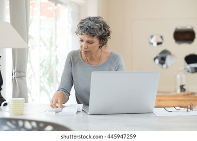 Senior Woman Working On Home Finance. Mature Woman Checking Bills At Home. Older Woman Checking Pension Approval Certificate With Laptop At Home.