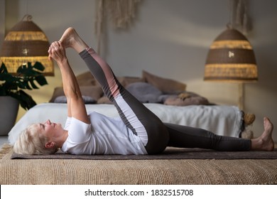 Senior Woman Working Out, Warming Up Using Yogic Belt, Lying In Yoga Supta Padangushthasana, One Leg Lift Exercise, Reclined Variation Of Extended Hand To Big Toe Pose At Home.