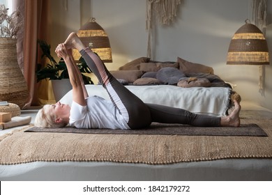 Senior Woman Working Out, Warming Up Using Yogic Belt, Lying In Yoga Supta Padangushthasana, One Leg Lift Exercise, Reclined Variation Of Extended Hand To Big Toe Pose At Home.