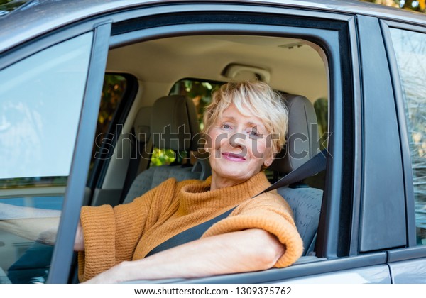 Senior\
woman working as taxi driver, smiling at\
camera.