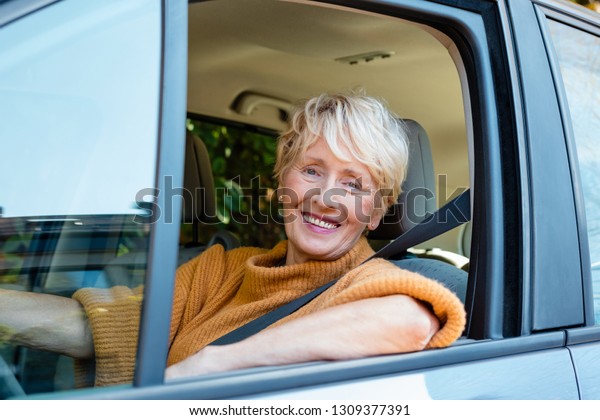 Senior\
woman working as taxi driver, smiling at\
camera.