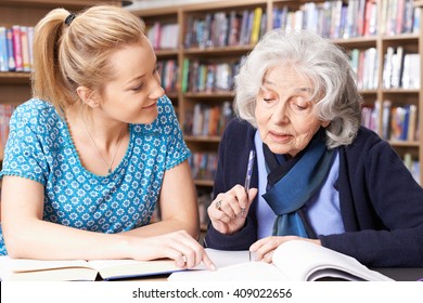 Senior Woman Working With Teacher In Library