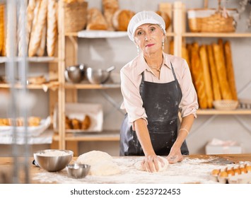 Senior woman works in bakery as baker, kneads dough, works with flour. Working moment, process of creating croissants in bakery - Powered by Shutterstock