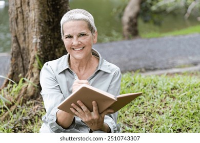 Senior Woman Writing in Journal Outdoors by a Tree Near a Lake on a Sunny Day - Powered by Shutterstock