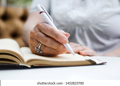Senior woman writing in note book.Old female hands on paper note writing down a memo for the day 