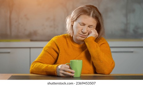 Senior woman yawns and naps during breakfast in apartment. Woman with short frizzy hair drinking hot coffee from cup to energize for day - Powered by Shutterstock