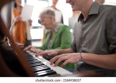 Senior woman with young teacher playing at piano in choir rehearsal.