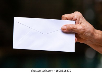 Senior Woman's Hand Holding White Envelope In Black Background, Close Up Shot, Business Concept