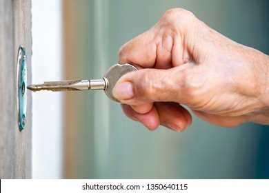 Senior Woman's Hand Use A Key For Lock Or Unlock Wooden Door, Close Up & Macro Shot, Selective Focus, Security Concept