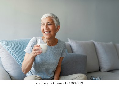 Senior woman's hands holding a glass of milk. Happy senior woman having fun while drinking milk at home. Senior Woman drinking a glass of milk to maintain her wellbeing.