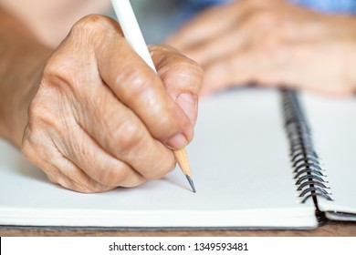 Senior Woman's Right Hand Writing Letter On Ivory Paper Background, Notebook, A White Pencil, Close Up & Macro Shot, Selective Focus, Stationery Concept