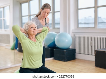 Senior women doing light pilates workout for back muscles with coach assistance. Trainer helping senior woman exercising at gym. - Powered by Shutterstock