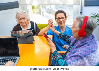 Senior women and nurse using technology in the geriatrics listening to music with cellphone and using digital tablet and laptop - Powered by Shutterstock