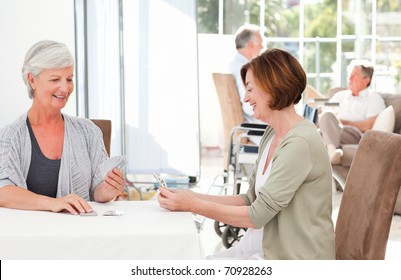 Senior Women Playing Cards While Their Husbands Are Talking