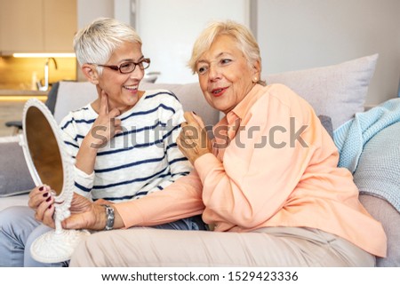 Senior women spending time together at home. Cheerful positive attractive senior lady friends looking at the mirror satisfied with nature beauty. Two cheerful senior women chatting at home. 