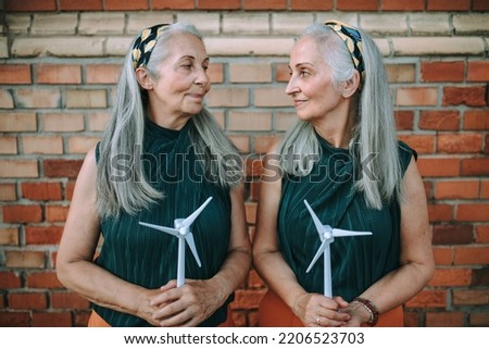 Senior women, twins holding plastic model of wind turbine, concept of future, ecology and renewable resources, message for next generation.