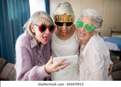 Senior women wearing novelty glasses making face while taking selfie through mobile phone at nursing home  - Powered by Shutterstock