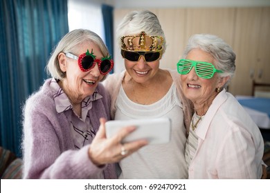 Senior women wearing novelty glasses taking selfie through smart phone at nursing home - Powered by Shutterstock