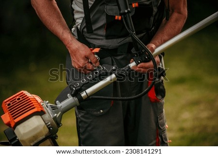 Senior worker preparing to use a lawn trimmer cutting grass in the natural background. Housework concept