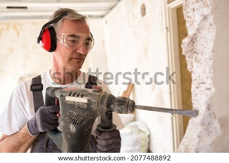 Senior worker using drill at contruction site, closeup