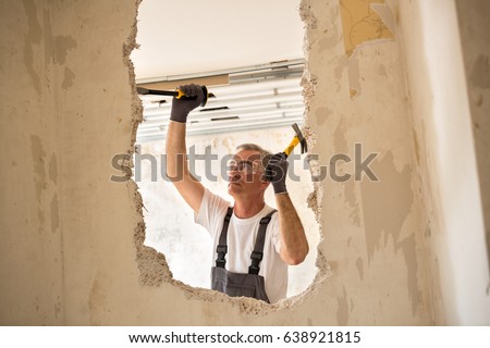 Senior worker using tool at contruction site, demolish wall