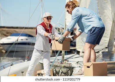 Senior yachtsman and his assistant loading boxes on boat before sailing trip on summer weekend - Powered by Shutterstock